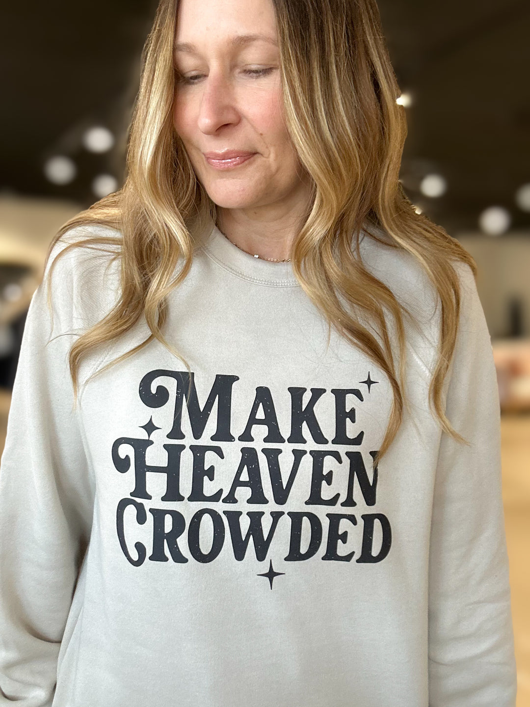 Woman wearing a white sweatshirt with 'MAKE HEAVEN CROWDED' text.