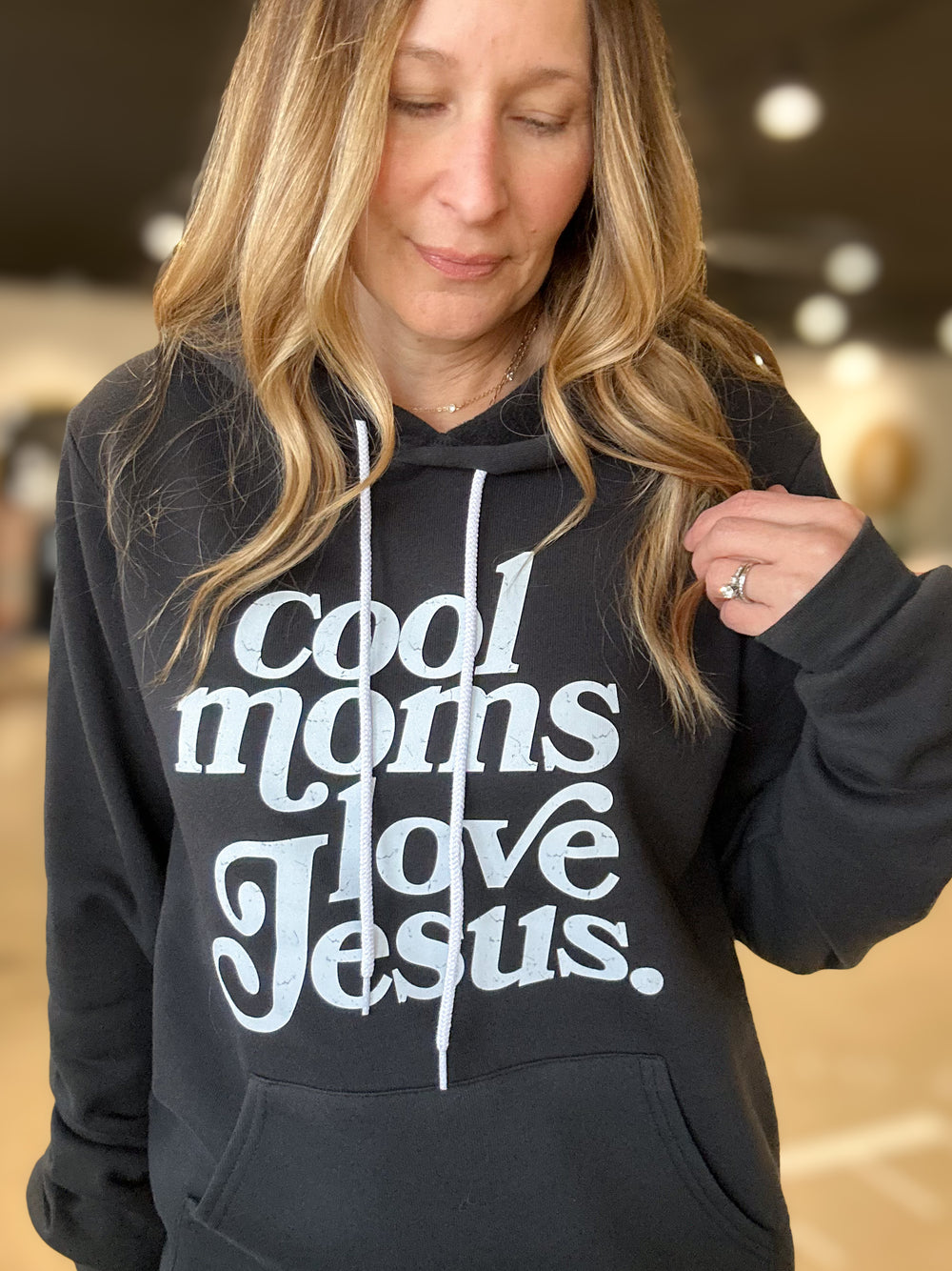 Person wearing a black hoodie with 'cool moms love Jesus' text.