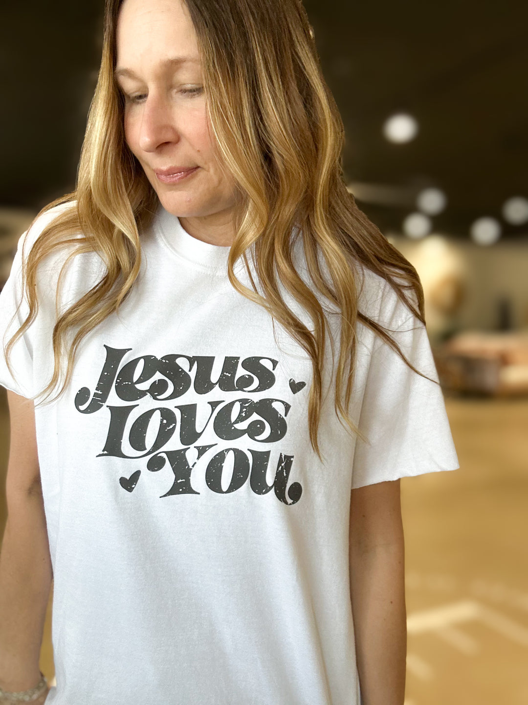 Woman wearing a white t-shirt with 'Jesus Loves You' text.