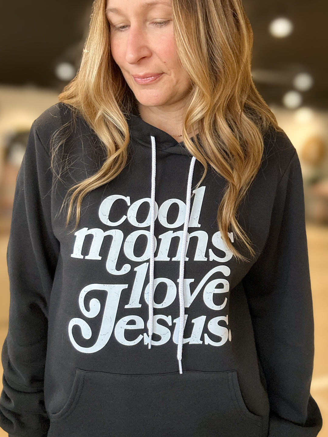 Person wearing a black hoodie with 'Cool moms love Jesus' text.