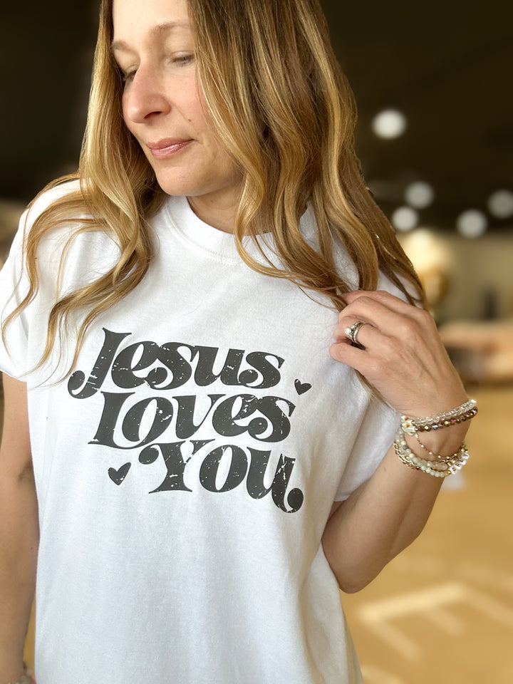 Woman wearing a white t-shirt with 'Jesus Loves You' text.