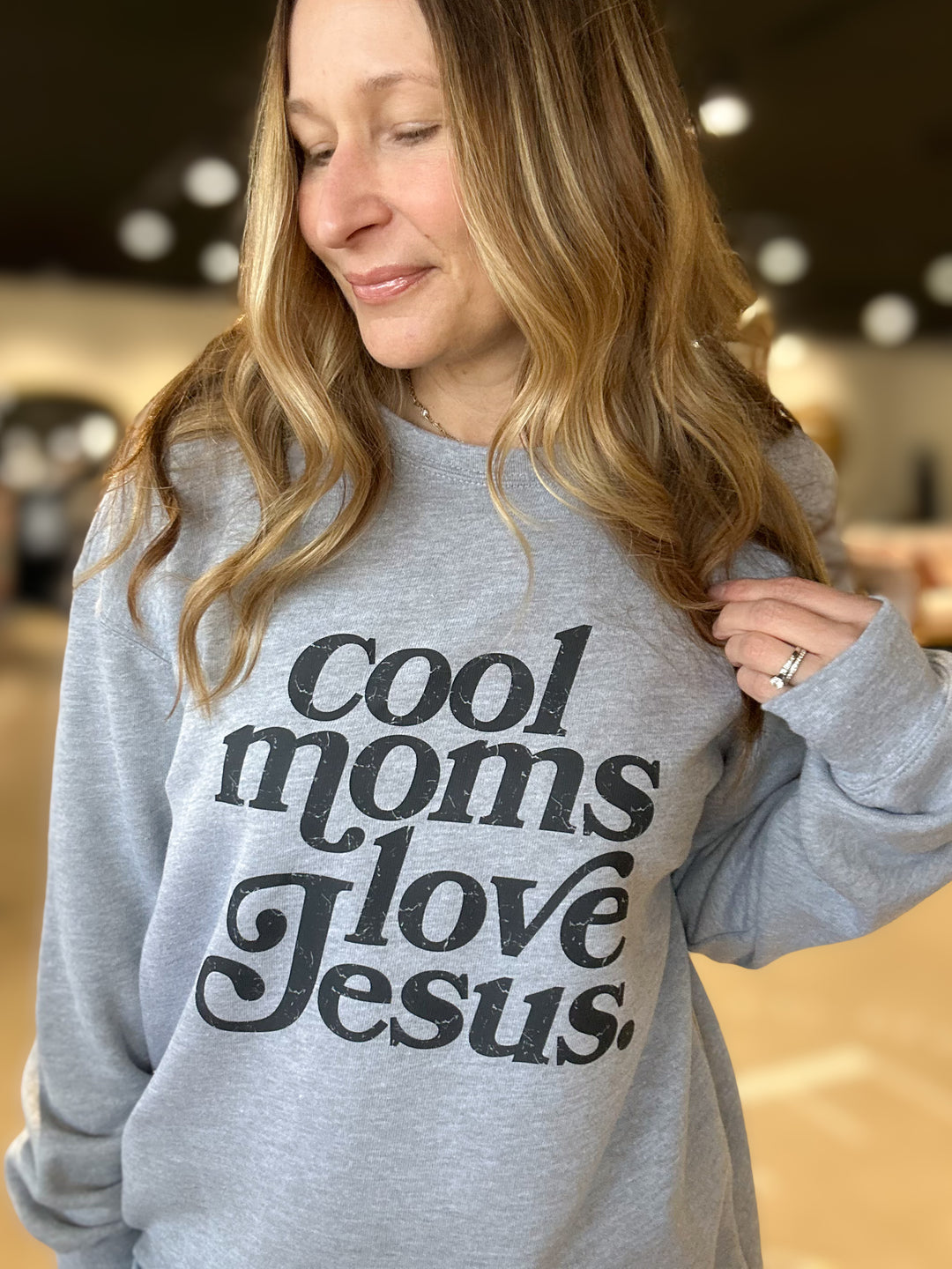 Person wearing a gray sweatshirt with 'Cool moms love Jesus' text.