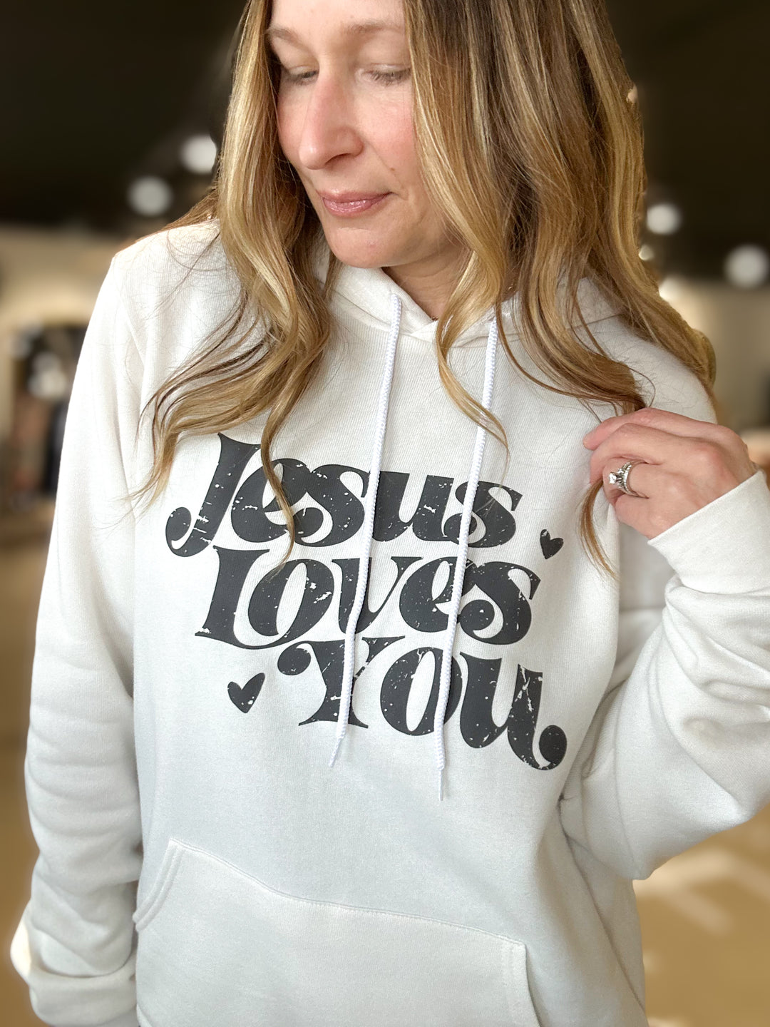 Person wearing a white hoodie with 'Jesus Loves You' text.
