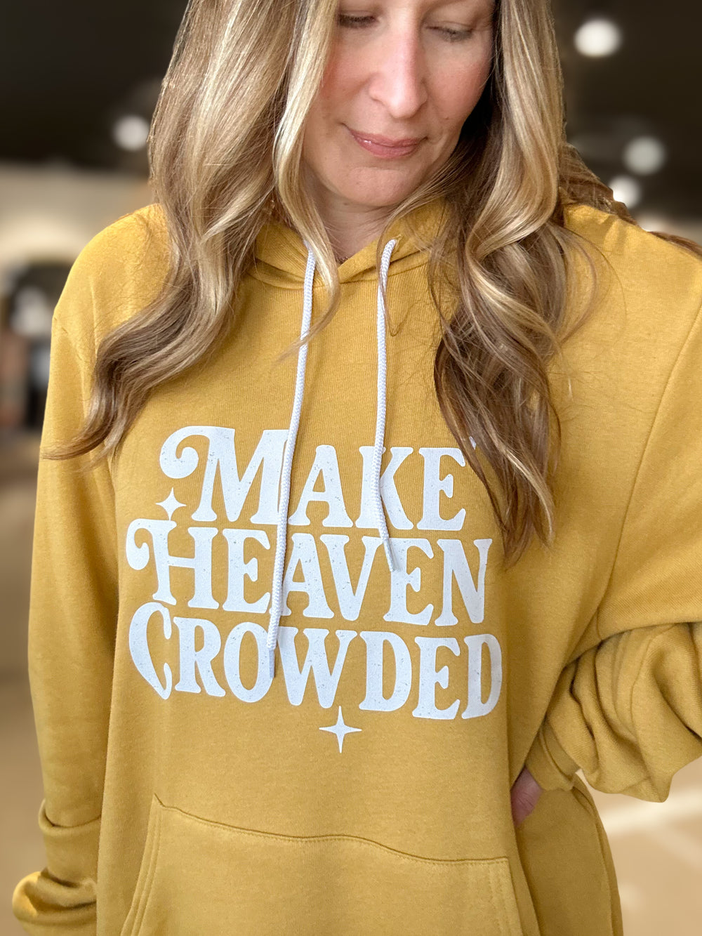 Person wearing a mustard yellow hoodie with 'MAKE HEAVEN CROWDED' text.