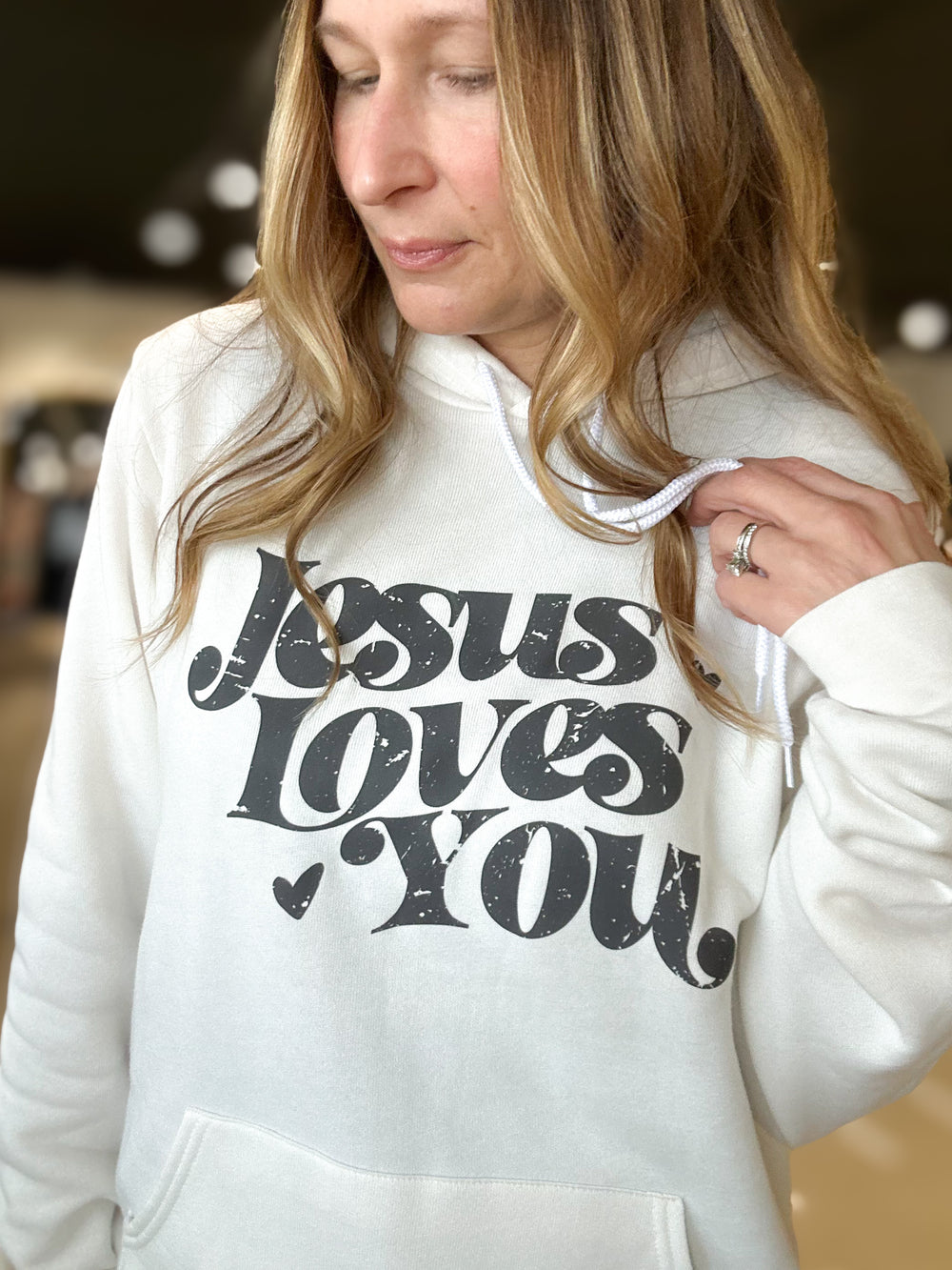 Person wearing a white hoodie with 'Jesus Loves You' text.