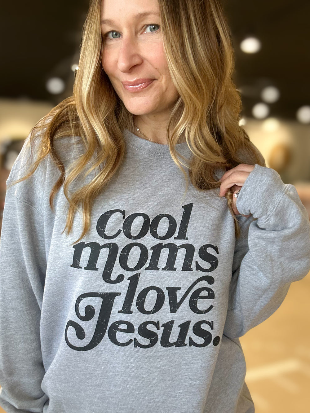 Person wearing a gray sweatshirt with 'Cool moms love Jesus' text.
