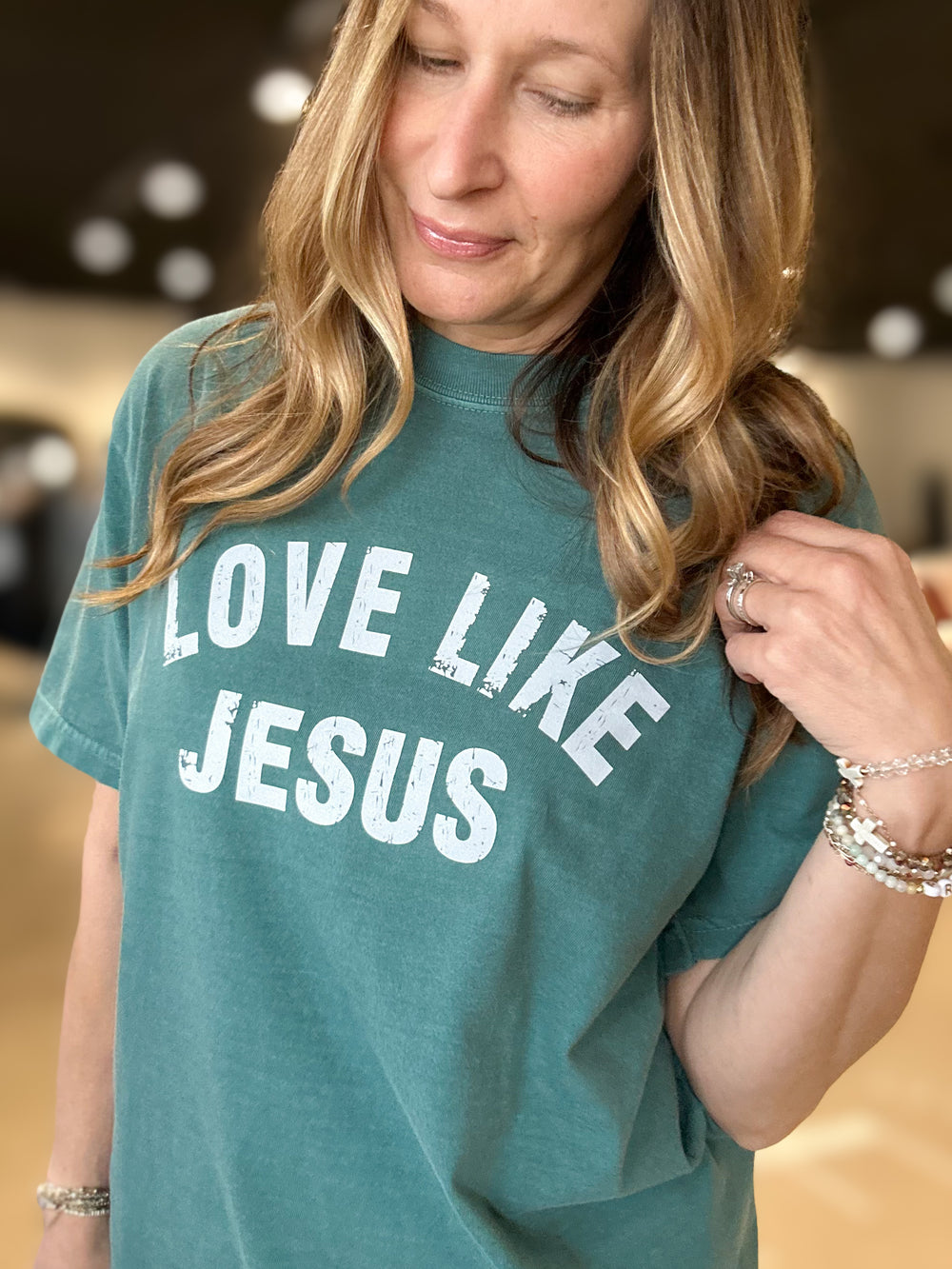 Woman wearing a teal t-shirt with 'LOVE LIKE JESUS' text.