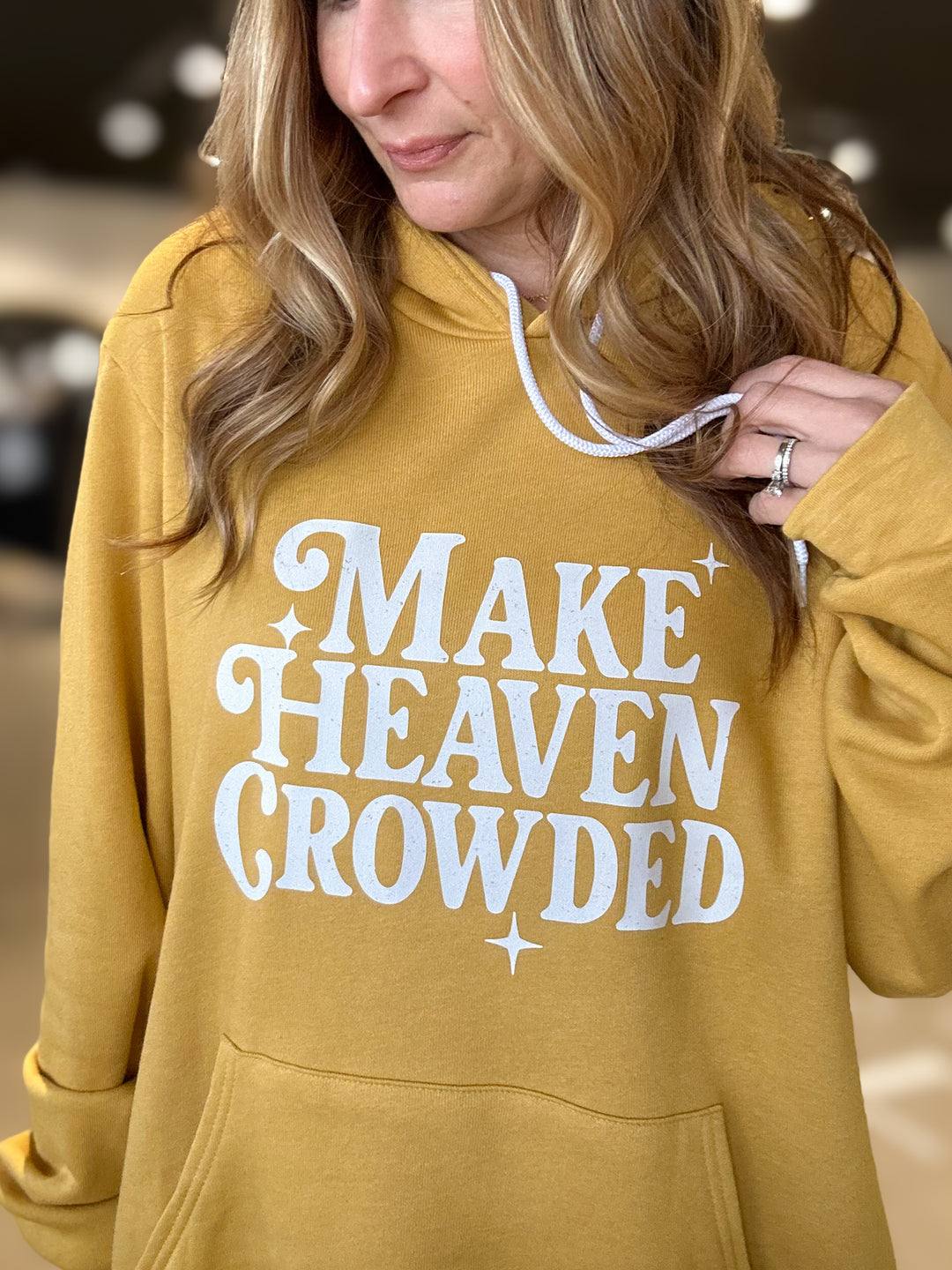 Person wearing a mustard yellow hoodie with 'MAKE HEAVEN CROWDED' text.
